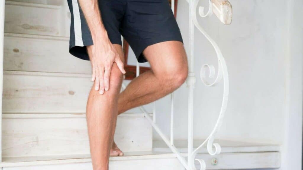 Pictuer of a person holding their painful knee while walking downstairs