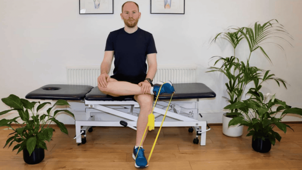 James McCormack sitting on a physio plinth, performing a strengthening exercise for the posterior tibial tendon